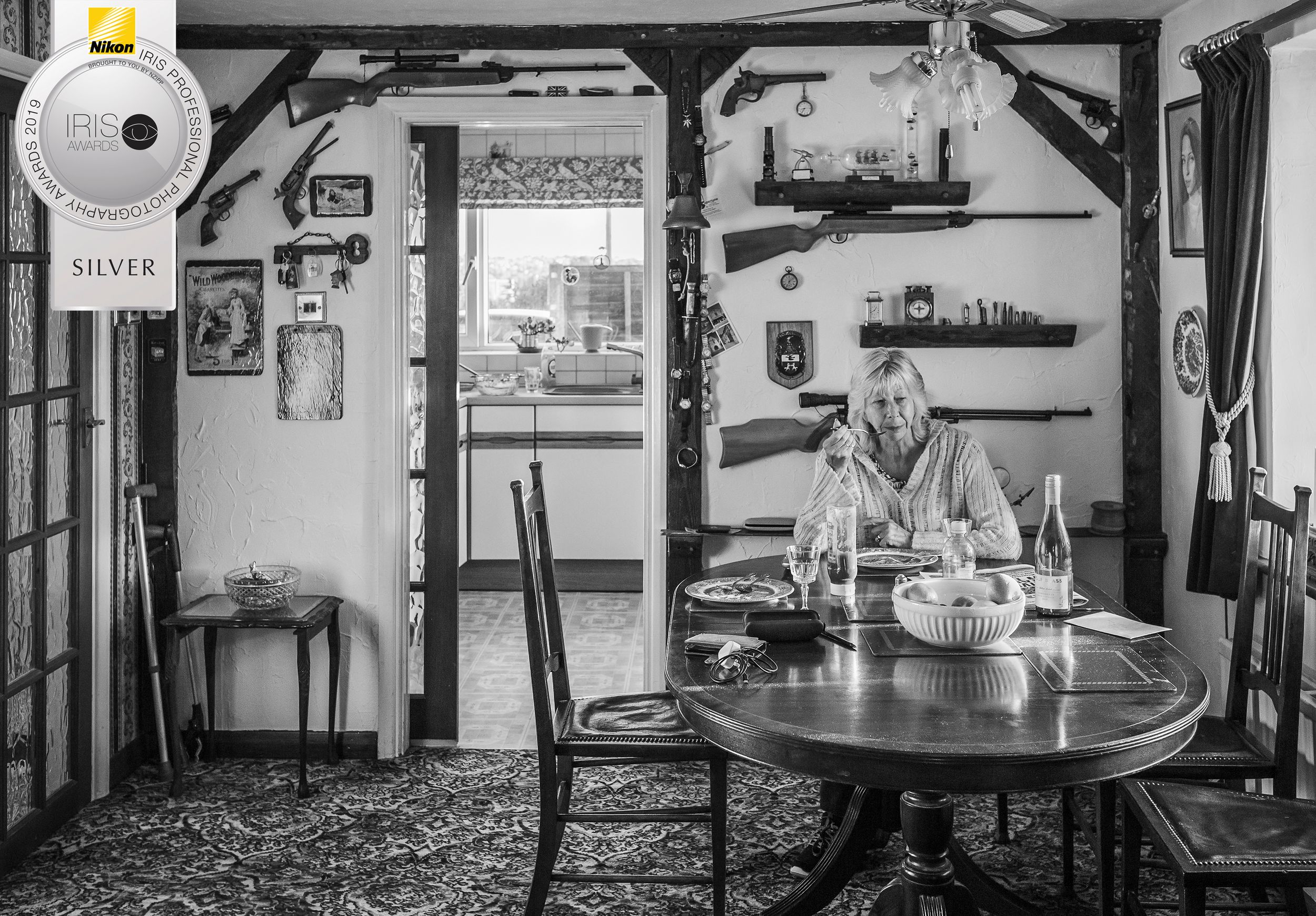 Woman eating dinner at table alone on house with guns on wall
